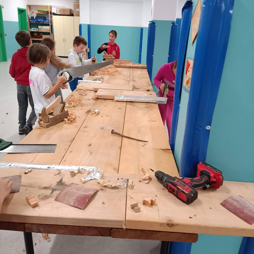 Bambini al banco da lavoro usano sega, carta abrasiva e utensili in un laboratorio pratico sul legno.