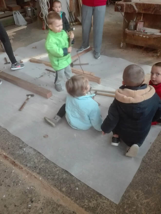 Bambini piccoli sperimentano legno e martelli in un laboratorio di falegnameria assistito.