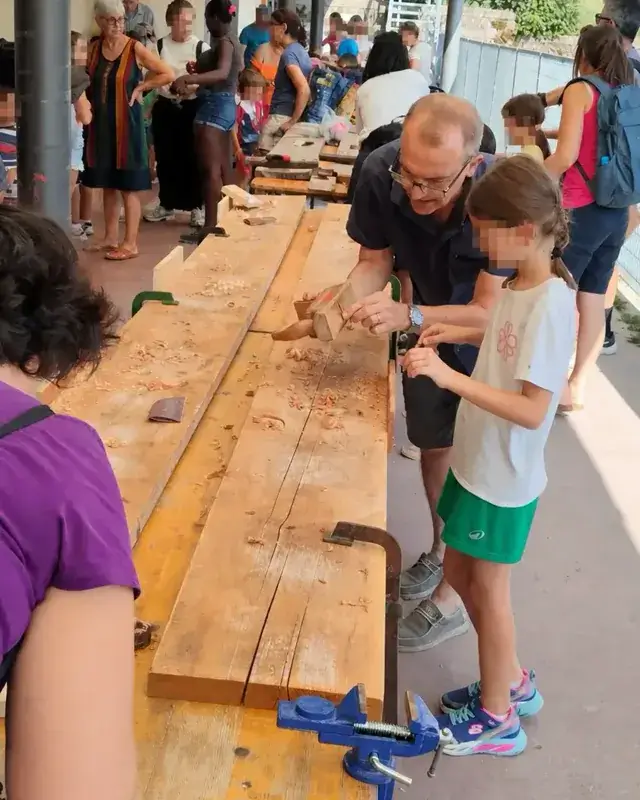 Una lunga tavolata riunisce bambini, genitori e volontari impegnati nella falegnameria.