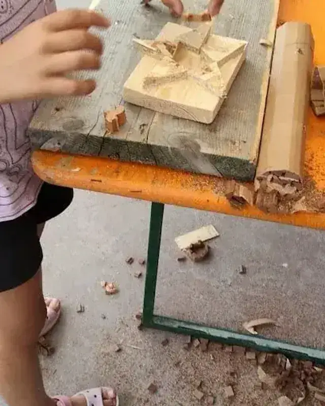Mani al lavoro su un piccolo TAU di legno, tra trucioli e utensili sul banco.