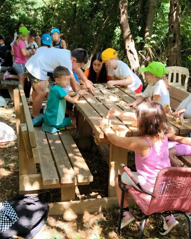 Un grande gruppo lavora intorno a un lungo tavolo nel bosco.
