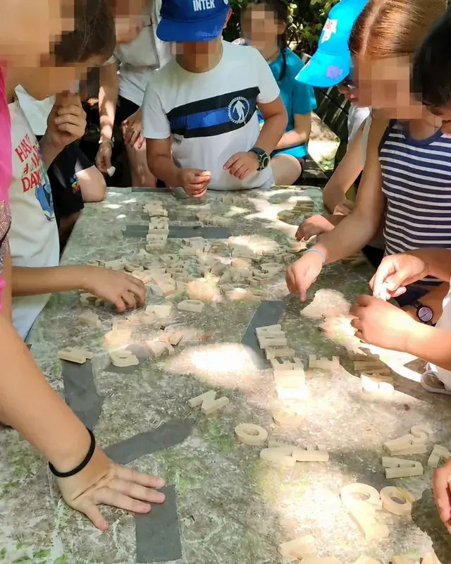 Bambini dispongono lettere e piccoli elementi di legno su un tavolo di pietra.