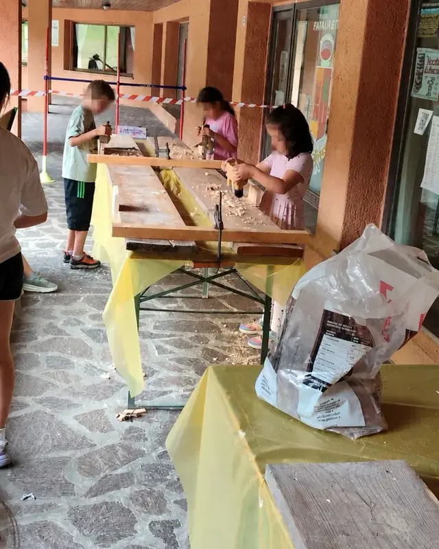 Tre bambini usano utensili manuali verticali su lunghe tavole di legno.