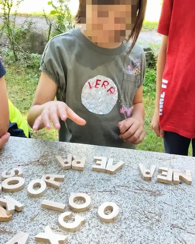 Una bambina compone una parola con lettere di legno disposte sul prato.