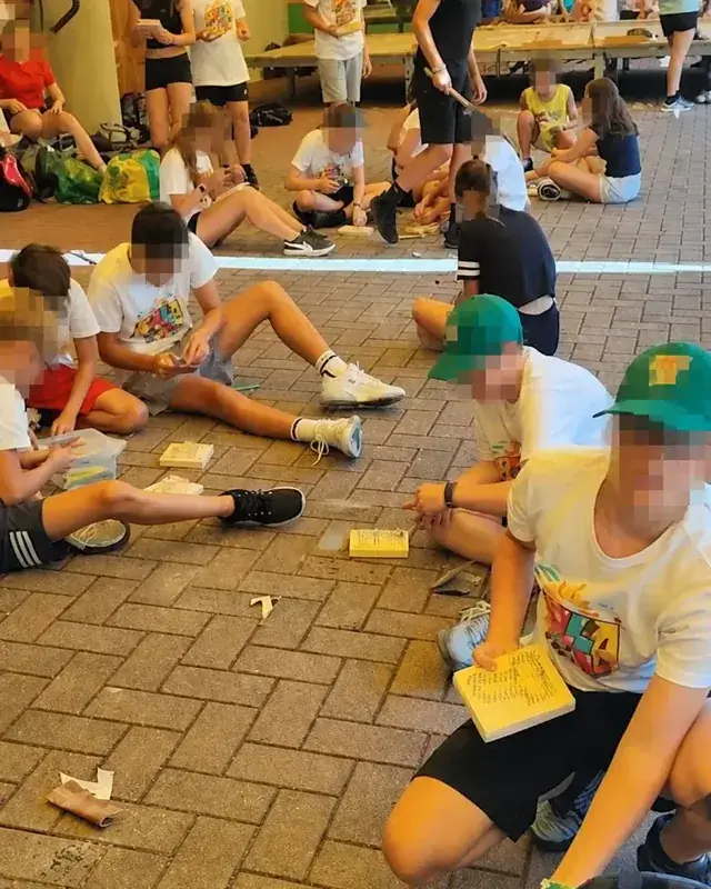 Diversi gruppi lavorano con legno e strumenti sotto il portico.