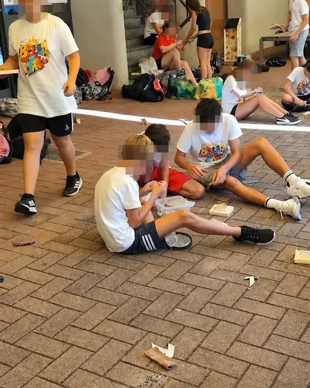 Ragazzi seduti in piccoli gruppi lavorano il legno nello spazio esterno.