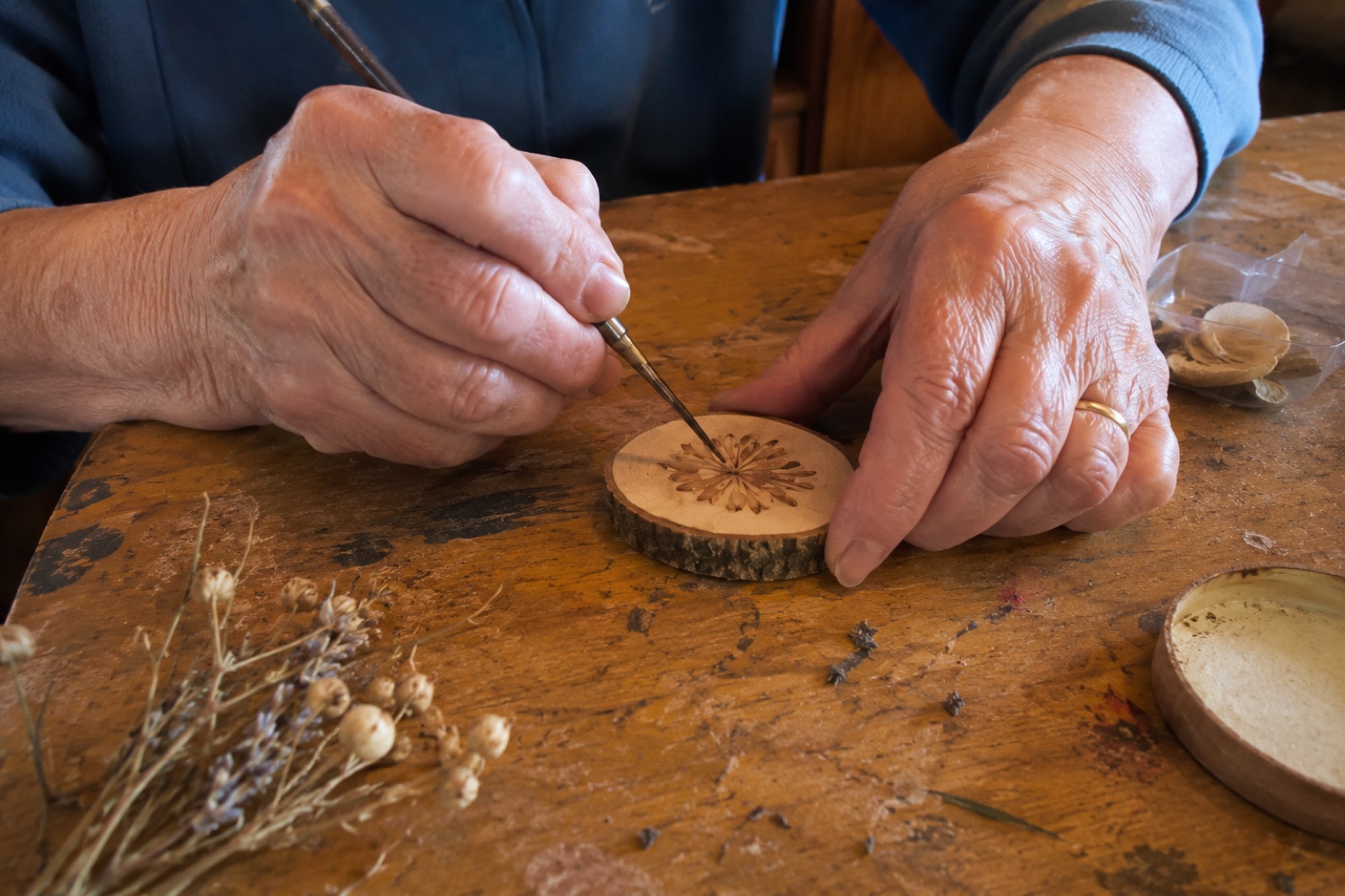 Mani di una persona anziana impegnate a decorare una sezione circolare di legno.